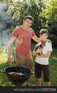 father son looking camera during cooking barbecue park