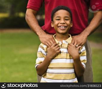 Father standing behind son with hands on his shoulders as boy smiles.