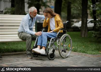 Father takes care of a disabled daughter in wheelchair, family walking in park. Paralyzed people and disability, handicap overcoming. Handicapped female person and adult male guardian in public place. Father takes care of a disabled daughter