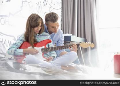 Father teaching daughter to play electric guitar at home