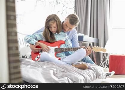 Father teaching daughter to play guitar at home