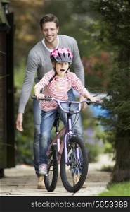 Father Teaching Daughter To Ride Bike In Garden