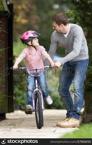 Father Teaching Daughter To Ride Bike In Garden