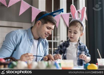 father teaching his son how paint eggs easter