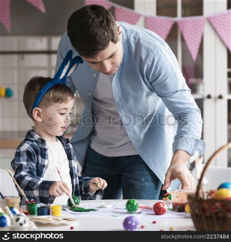 father teaching little boy how paint easter eggs