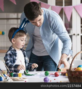 father teaching little boy how paint easter eggs