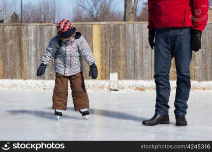 Father teaching son how to ice skate at an outdoor skating rink in winter.