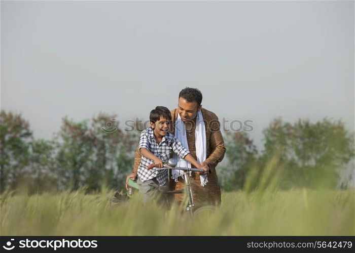 Father teaching son to ride cycle in the field