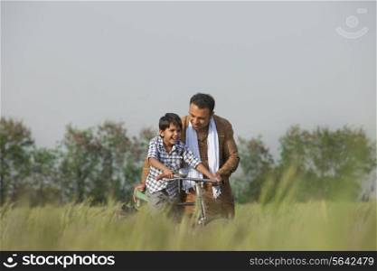 Father teaching son to ride cycle in the field