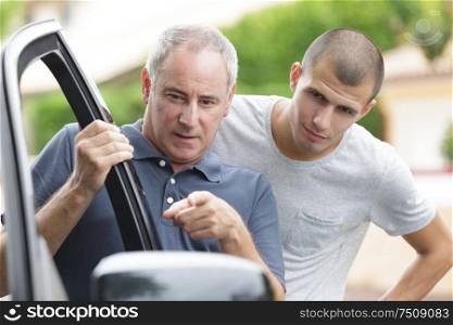 father teaching teenage son about a car