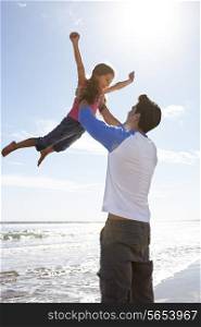 Father Throwing Daughter Into Air On Beach