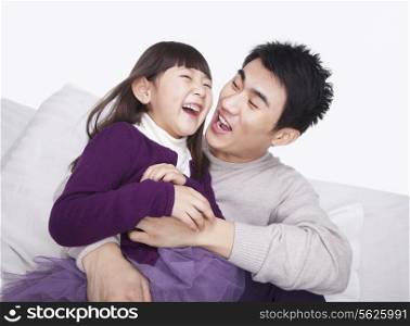 Father tickling daughter on the sofa, studio shot