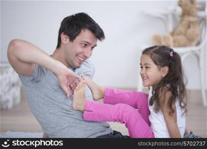 Father tickling daughter&rsquo;s foot at home