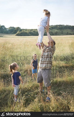 Father tossing little girl in the air. Family spending time together on a meadow, close to nature. Parents and children playing together. Candid people, real moments, authentic situations