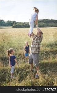 Father tossing little girl in the air. Family spending time together on a meadow, close to nature. Parents and children playing together. Candid people, real moments, authentic situations