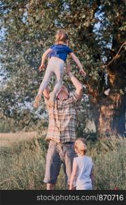 Father tossing little girl in the air. Family spending time together on a meadow, close to nature. Parents and children playing together. Candid people, real moments, authentic situations