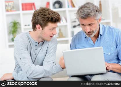 Father using laptop, teenage son next to him
