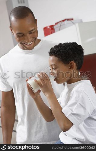 Father watching son (7-9) drinking milk, indoors