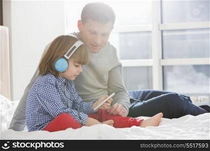 Father with boy listening music on headphones in bedroom
