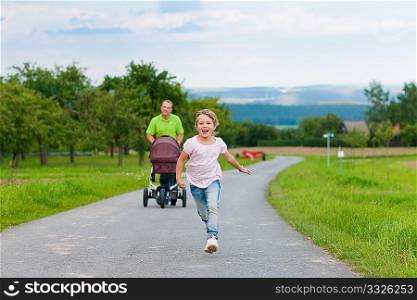 Father with child and a baby lying in a baby buggy walking down a path outdoors