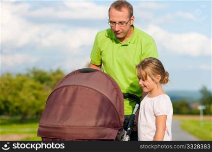Father with child and a baby lying in a baby buggy walking down a path outdoors