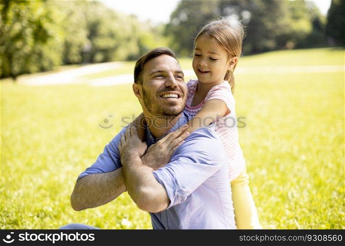 Father with cute little daughter having fun on the grass at the park