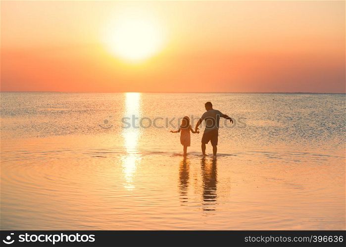 father with daughter walking by the calm sea at the sunset time