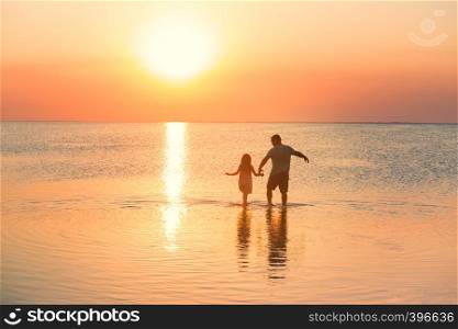 father with daughter walking by the calm sea at the sunset time
