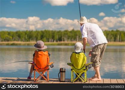 Father with his son and daughter on a wooden pier in the lake fishing with fishing rods