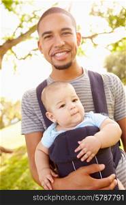 Father With Son In Baby Carrier Walking Through Park