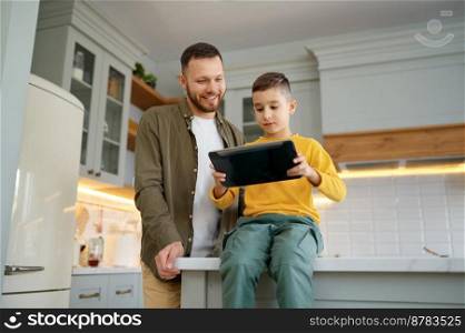 Father with son using digital tablet together at kitchen. Happy parent and child watching show or educational video spend fun time at home. Father with son using digital tablet together at home kitchen