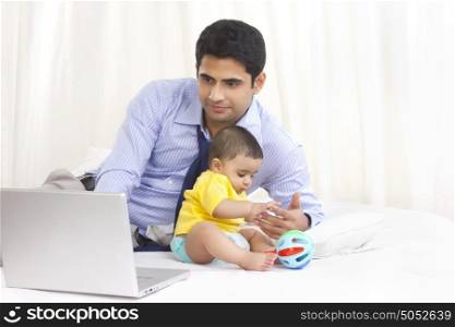 Father working on laptop while baby plays