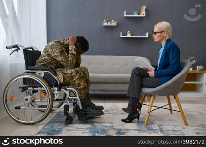 Fatigue soldier in wheelchair holding head in clenched hands. Therapy session at psychologist. Soldier in camouflage holding head in hands