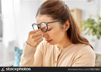 fatigue, stress, vision and people concept - tired asian woman with glasses rubbing nose bridge at home. tired asian woman with glasses rubbing nose bridge
