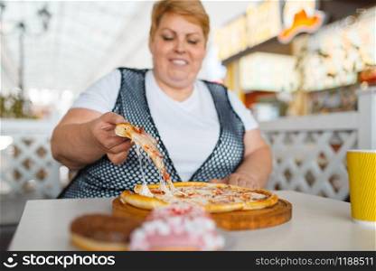 Fatty woman eating pizza in fastfood restaurant, unhealthy food. Overweight female person at the table with junk dinner, obesity problem
