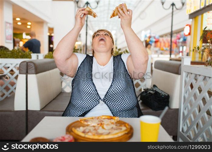 Fatty woman eating pizza in mall restaurant, unhealthy food. Overweight female person at the table with junk dinner, obesity problem