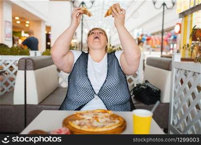 Fatty woman eating pizza in mall restaurant, unhealthy food. Overweight female person at the table with junk dinner, obesity problem