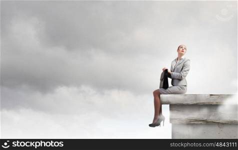 Fearless businesswoman with suitcase sitting on building top. Taking break from office