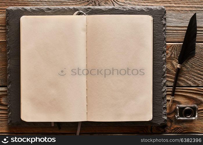Feather pen and blank notebook page over wooden background