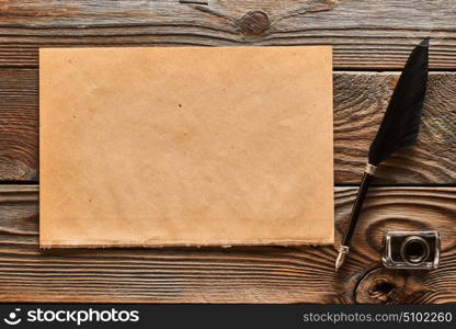 Feather pen and blank paper sheet over wooden background