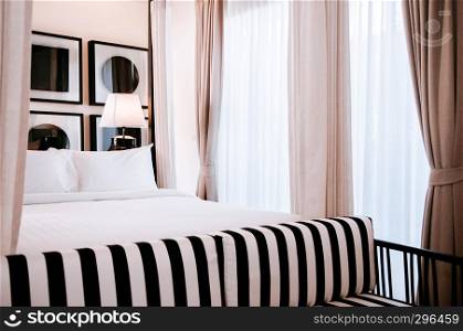 FEB 10, 2014 Chiang Mai, THAILAND - Asian contemporary hotel bedroom with wooden four poster bed with curtain, white sheet, Black and white strips pattern armchair, lamp and modern wall picture frames
