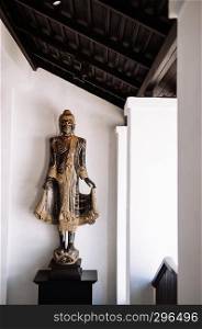 FEB 10, 2014 Chiang Mai, THAILAND - Beautiful old carved wood standing Buddha sculpture, Lanna northern Thai style antique Buddha with white wall background