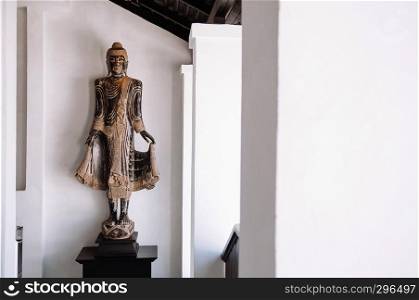 FEB 10, 2014 Chiang Mai, THAILAND - Beautiful old carved wood standing Buddha sculpture, Lanna northern Thai style antique Buddha with white wall background