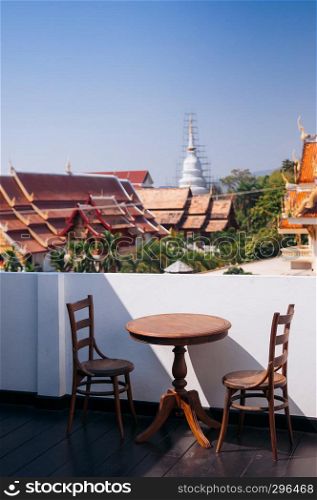 FEB 10, 2014 Chiang Mai, THAILAND - Vintage old wooden round dining table and chair at outdoor hard wood floor balcony, white wall with old temple view and blue sky