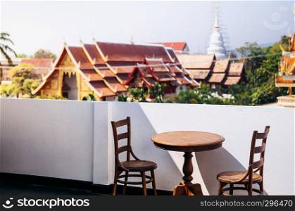 FEB 10, 2014 Chiang Mai, THAILAND - Vintage old wooden round dining table and chair at outdoor hard wood floor balcony, white wall with old temple view