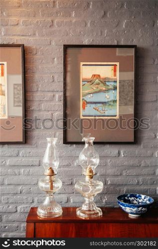 FEB 12, 2014 Chiang Mai, Thailand - Vintage glass kerosene lamps and antique ceramic pedestal tray with grey brick wall background, Asian retro home decoration items