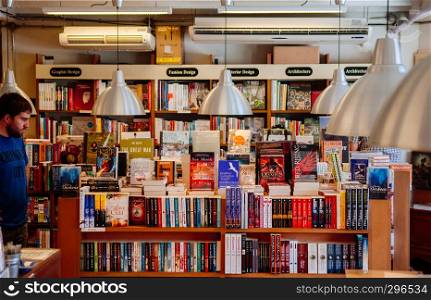 FEB 12, Chiang Mai, THAILAND - Male European customer among various book collections on wooden shelf with large modern lamp hanging above in small bookstore