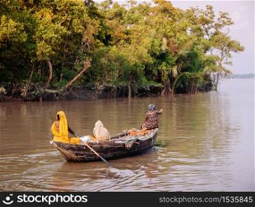 FEB 15, 2012 Dhaka, Bangladesh - Bangladesh local people on wooden row boat in river with tropical mangrove forest. Poverty social in South Asia