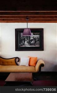 FEB 25, 2014 Dalat, Vietnam - Vintage colonial tropical country house living room hard wood floor classic sofa couch, pedant lamps and old picture frame on white wall