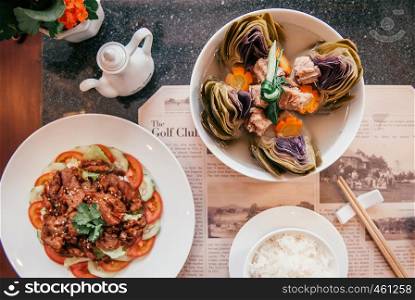 FEB 26, 2014 Dalat, Vietnam - Clear artichoke soup with pork rib and fried pork dish with rice in white bowl on newspaper designed dish mat. Vietnamese cuisine luch set in good restaurant. Top view